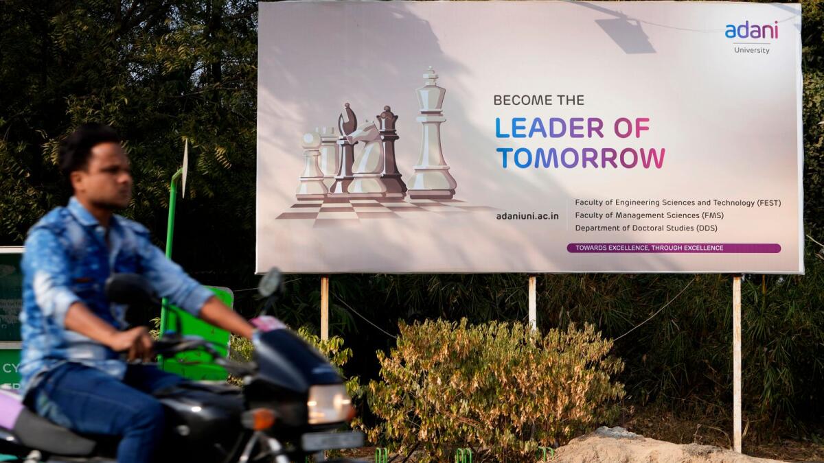 A motorist rides past a hoarding of Adani University near the corporate headquarters of Adani Group in Ahmedabad, India. Hindenburg said that Adani companies had “substantial debt” and that shares in seven Adani listed companies have an 85 per cent downside due to what it called “sky-high valuations”. — AP