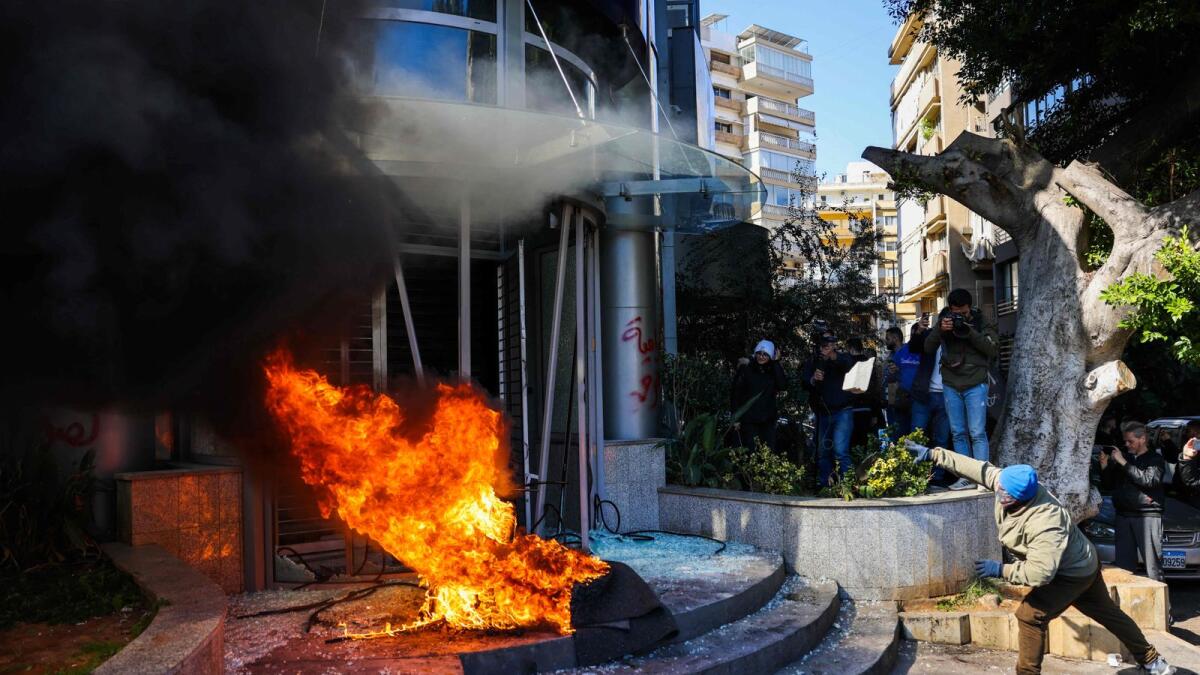 A protester throws a brick at a bank after setting fire to tyres during a demonstration in Beirut on Thursday. — AFP