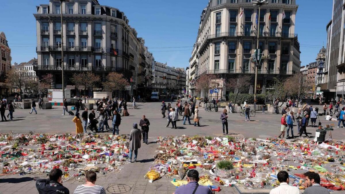 People sit on steps in front of the makeshift memorial for victims of the March 22, 2016 terror attacks at the Place de la Bourse (Beursplein) in Brussels.