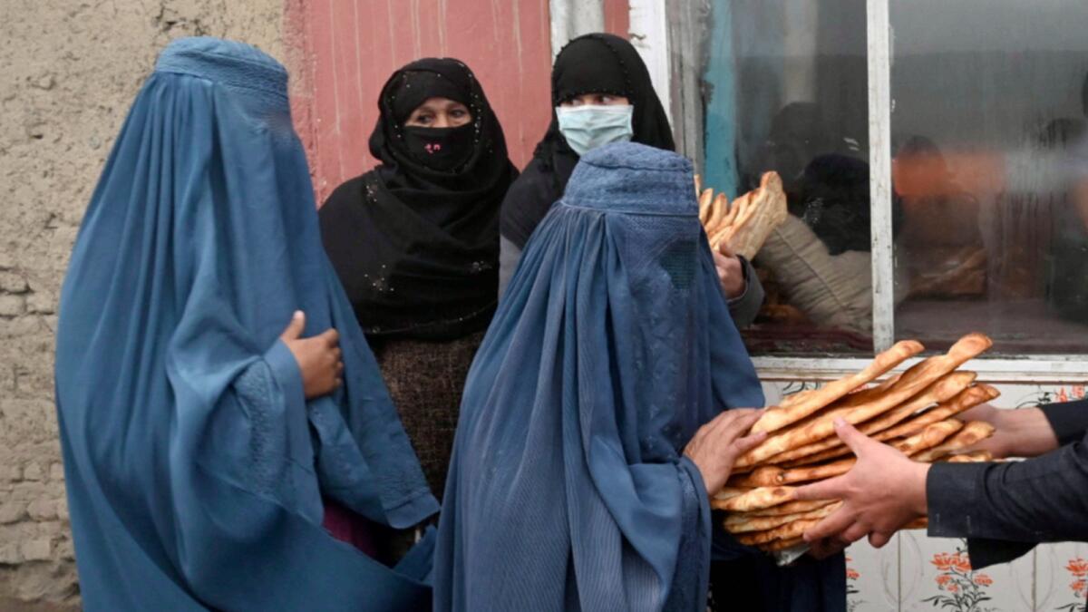 Women wearing a burqa receive free bread distributed as part of the Save Afghans From Hunger campaign in front of a bakery in Kabul. — AFP