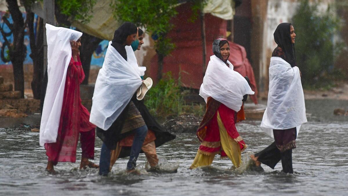 Women wade through a flooded street during a monsoon rainfall in Karachi on July 24, 2022. Photo: AFP