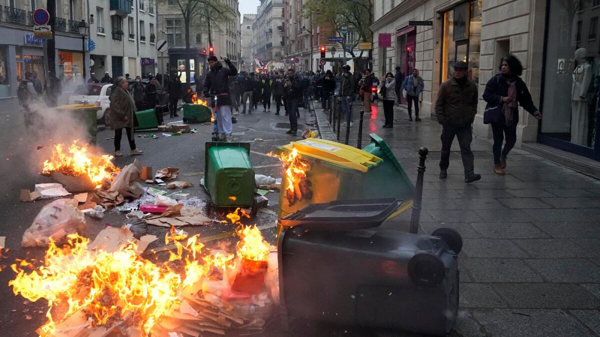 People walk by burning garbage cans during a protest, on Friday in Paris. — AP