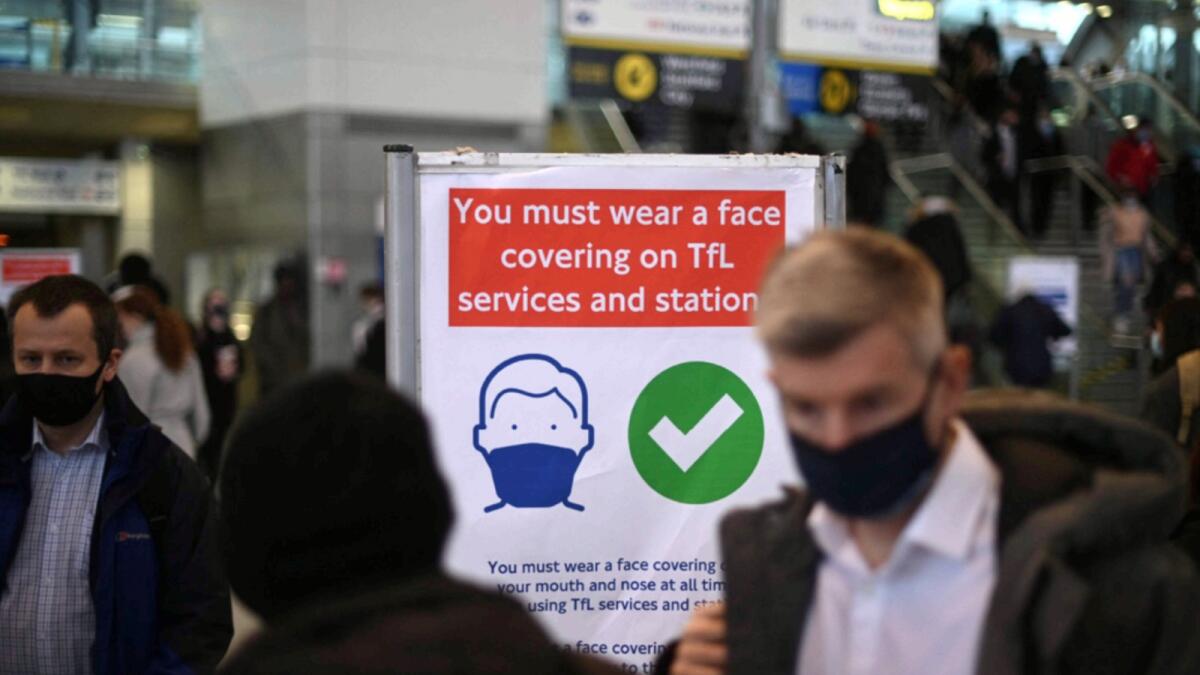Commuters walk past a notice board reminding them of wearing face coverings at Stratford underground station in east London. — AFP