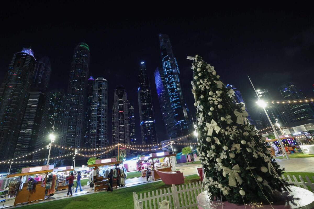 People take a stroll near a Christmas tree beneath the Dubai skyline on December 15, 2023.  — AFP