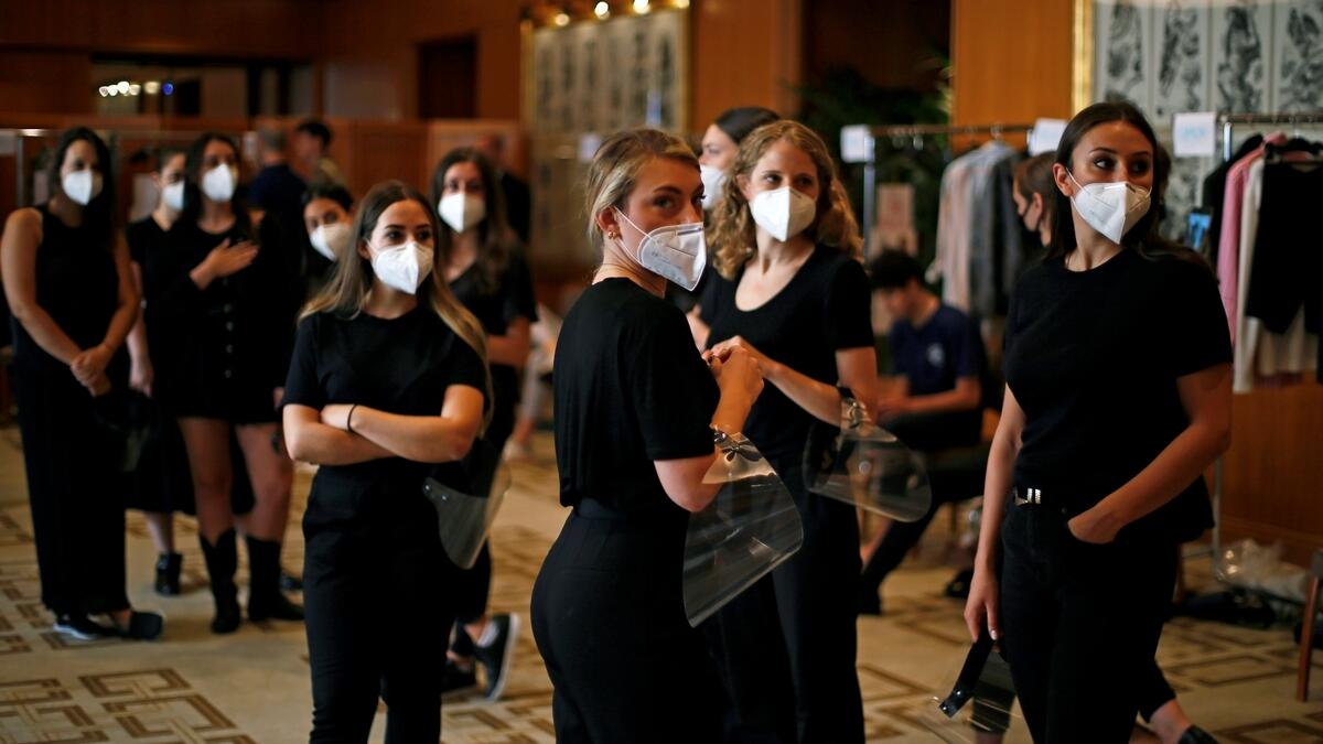 Dressers seen backstage with the mandatory masks on to assist the models before heading out for the show.