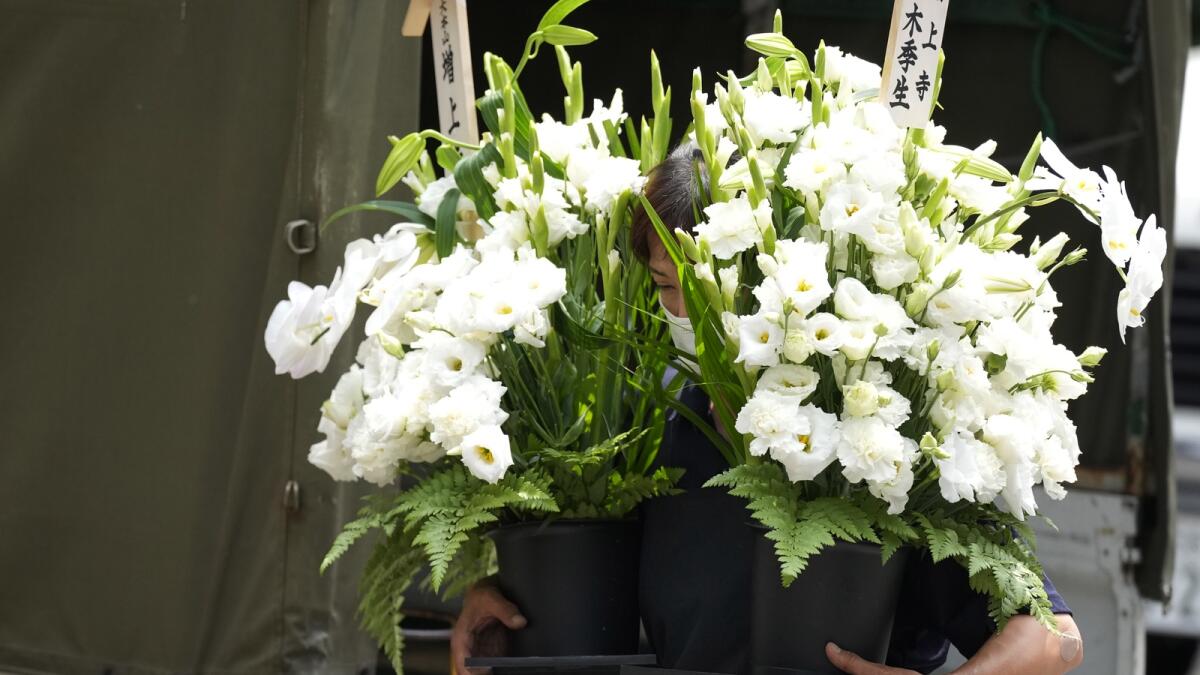 A worker brings a condolence flower to the residence of Japan's former Prime Minister Shinzo Abe. Photo: AP
