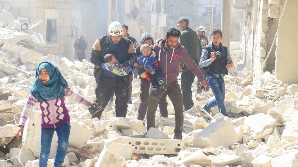 People and a civil defence personnel carry children at a damaged site after an air strike on rebel-held Idlib city. - Reuters
