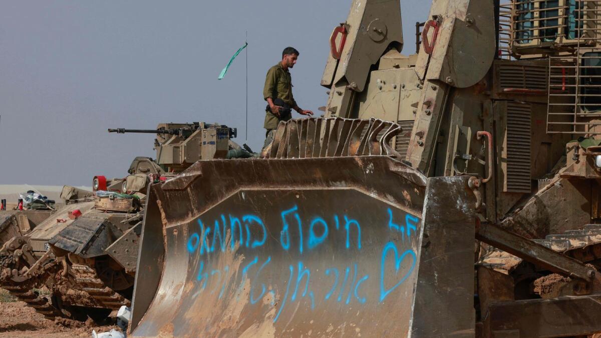 Israeli troops and military vehicles are positioned near the border with the Gaza Strip on Sunday. The graffiti in blue reads : “Our mission is to destroy Hamas”. - AFP