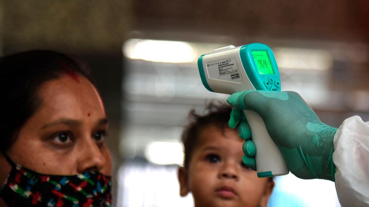 A health worker (R) checks the body temperature of a train passenger during a Covid-19 coronavirus screening at a railway terminus in Mumbai on December 14, 2020.  AFP