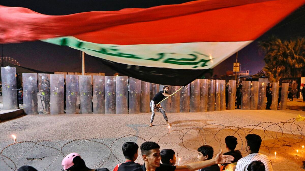 A protester waves an Iraqi flag while Security forces surround the protest site during ongoing anti-government protests in Basra, Iraq.