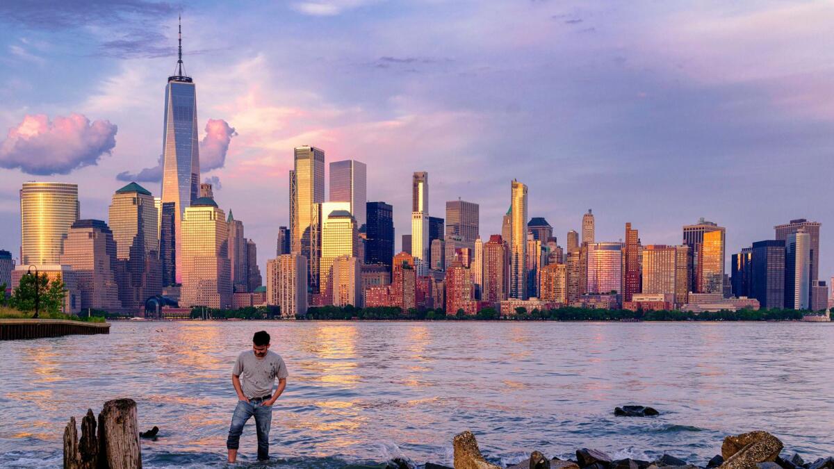 A man checks his footing as he wades through the Morris Canal Outlet in Jersey City, N.J., as the sun sets on the lower Manhattan skyline of New York City, on May 31, 2022. -- AP