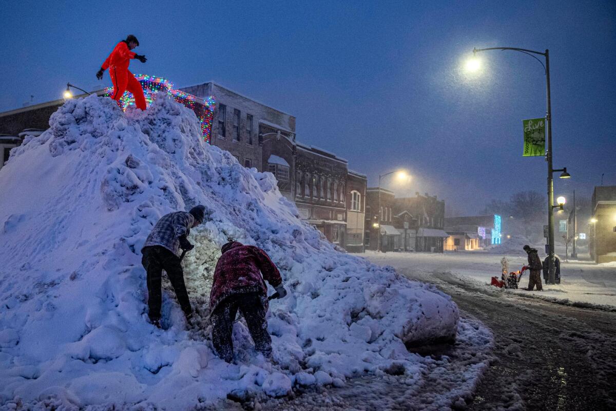 People stand on a large snow pile in Oskaloosa, Iowa, on Tuesday as another person uses a snow blower . — AP
