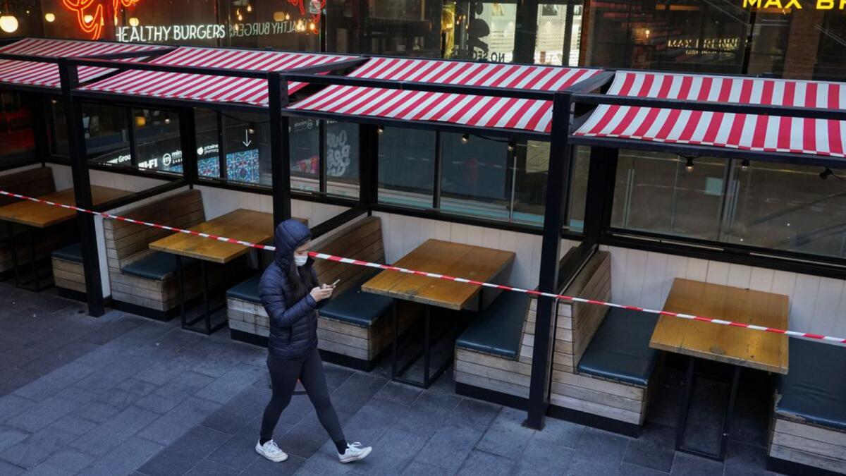 A woman wearing a protective mask walks past city centre restaurant tables closed to seating in accordance with public health regulations during a lockdown to curb the spread of  Covid-19 in Sydney. Reuters