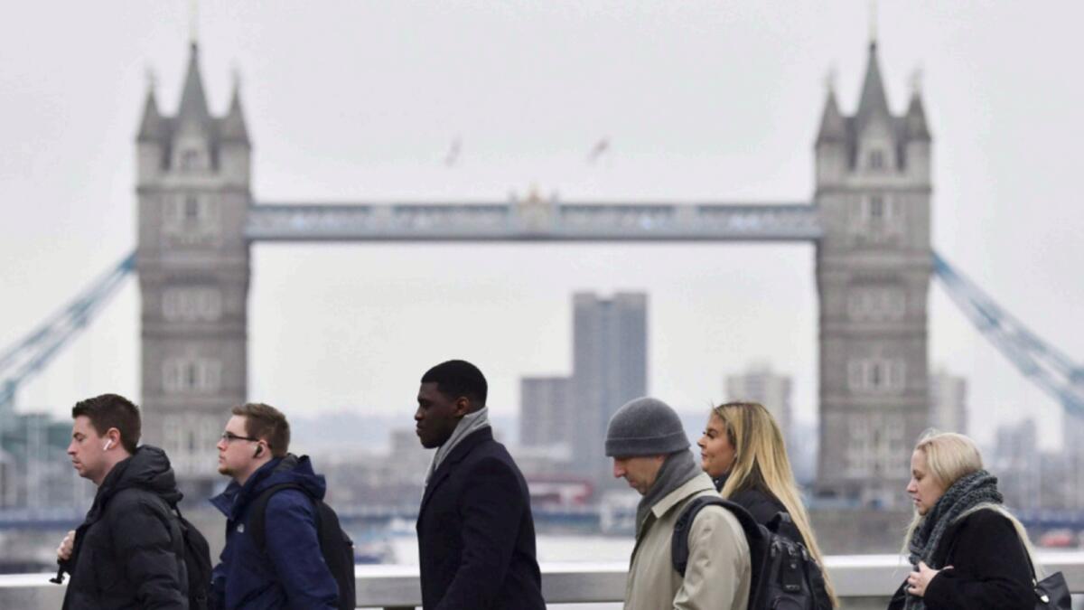 Pedestrians on their way to work cross the London Bridge backdropped by the Tower Bridge in central London after the Covid-19 restrictions were lifted in the UK. — AFP