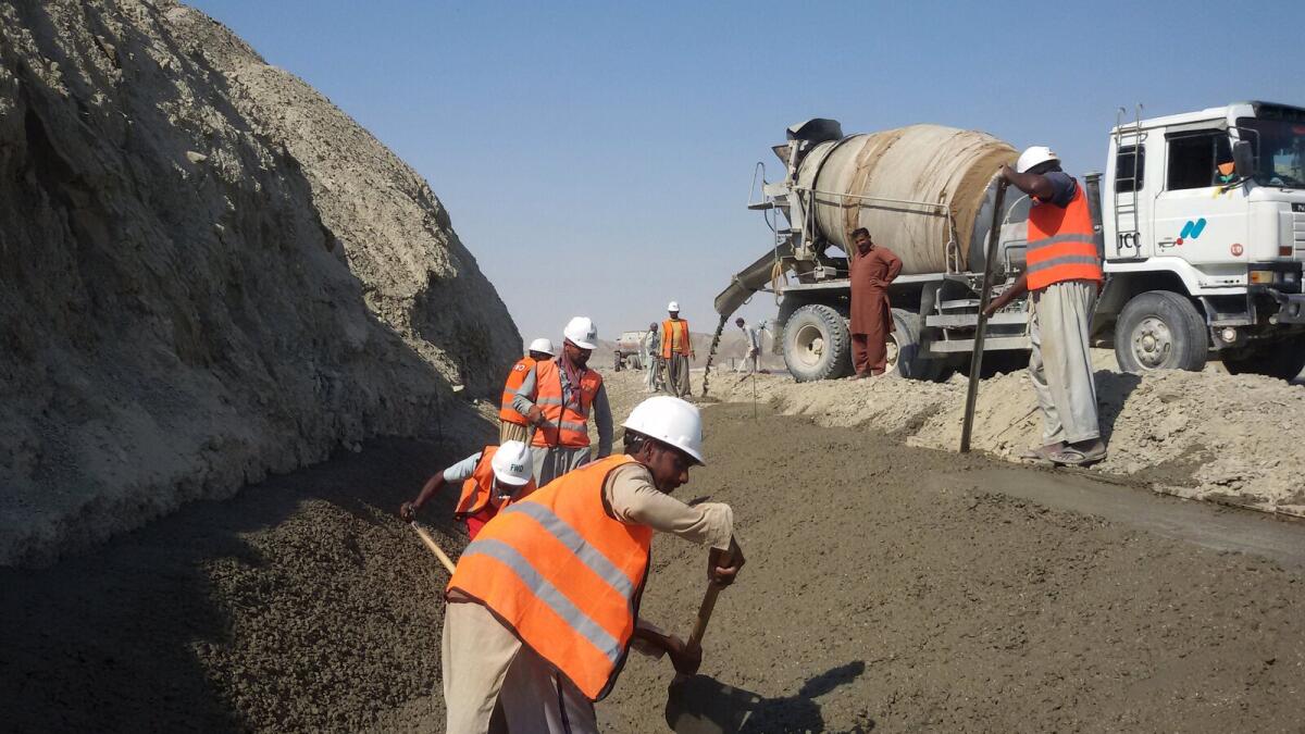 Labourers work on the development site of a storm water drain along a newly-constructed road on the outskirts of Gwadar; and, a worker tightens the wheels on a truck carrying a shipping container outside Quetta.