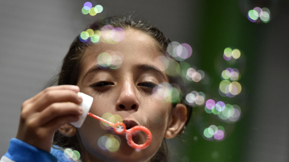 A migrant girl blows bubbles at a hall in Dortmund, Germany, Sunday, Sept. 6, 2015. Thousands of migrants and refugees arrived in Dortmund by trains. (AP Photo)