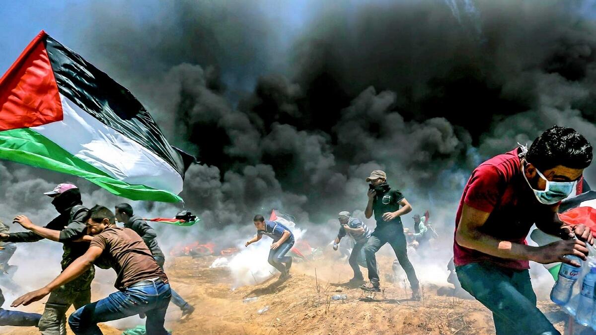 Palestinians run for cover from Israeli fire and teargas during a protest against the US embassy move to Occupied Jerusalem at the Israel-Gaza border on Monday. — Reuters