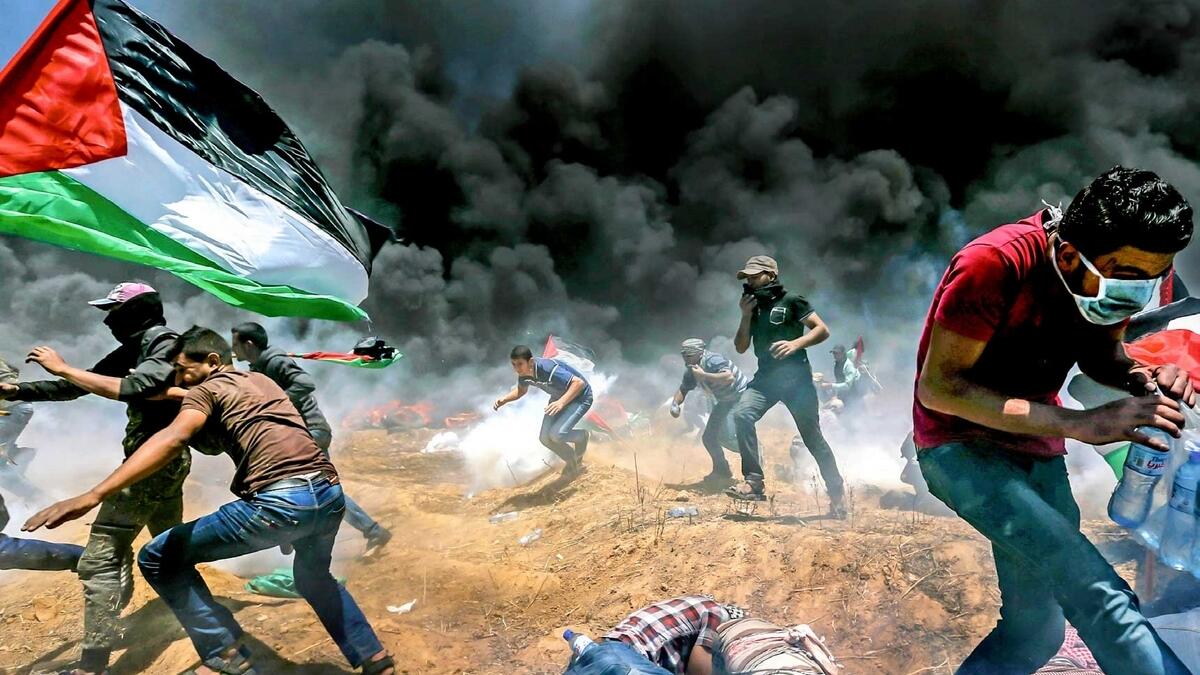Palestinians run for cover from Israeli fire and teargas during a protest against the US embassy move to Occupied Jerusalem at the Israel-Gaza border on Monday. — Reuters
