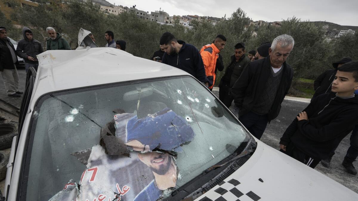 Palestinians look at a damaged car following an Israeli raid in the West Bank village of Jaba. — AP
