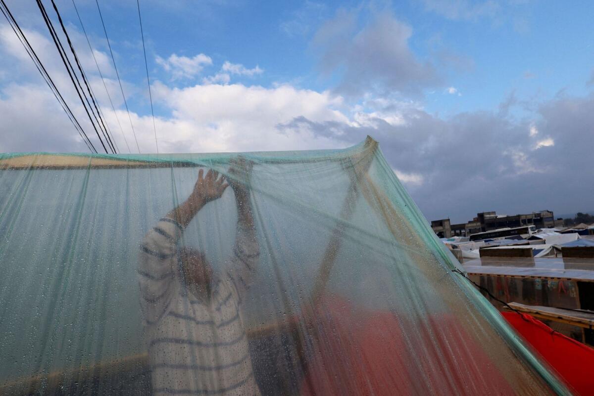 A displaced Palestinian adjusts his tent following heavy rains