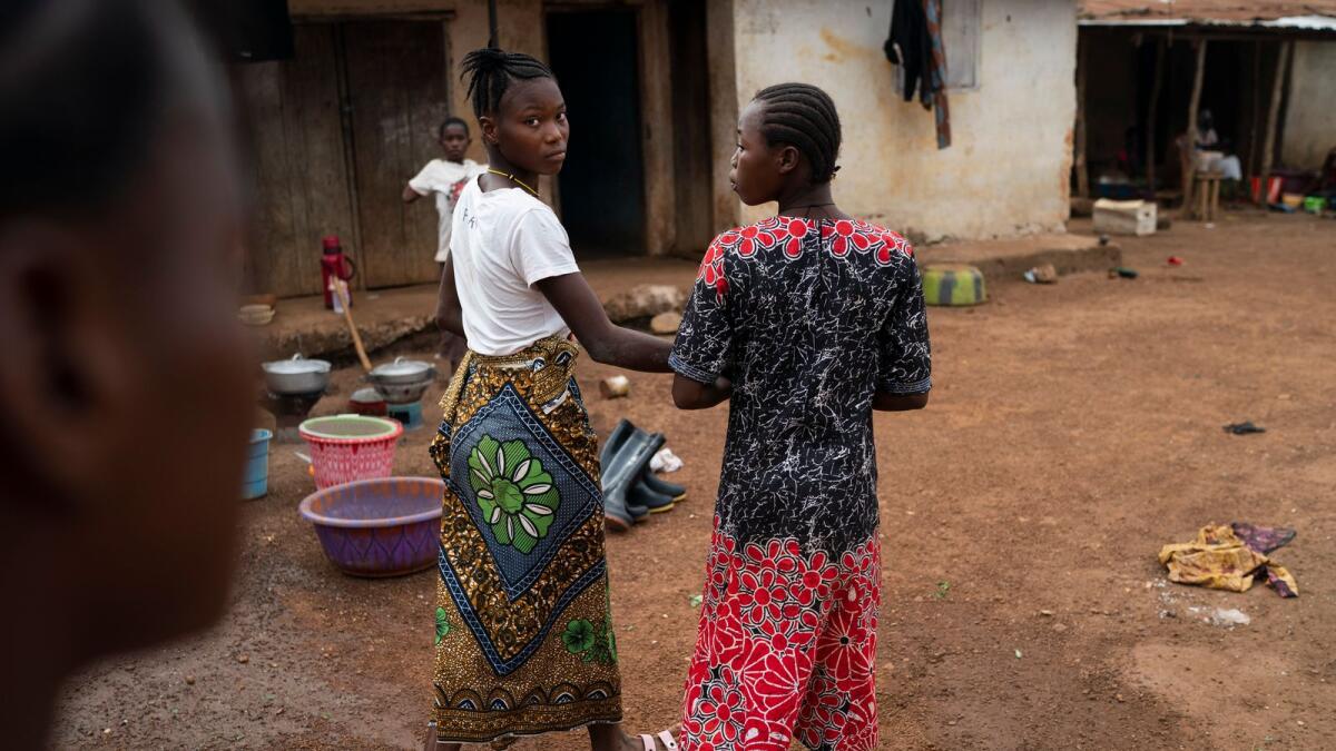 Marie walks with a friend on a street in Komao village, on the outskirts of Koidu, district of Kono, Sierra Leone.