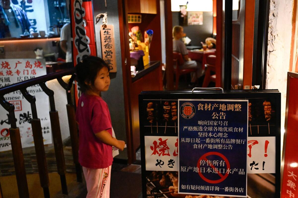 A girl is seen at an area of Japanese restaurants next to a sign reading 'Suspend the sale of all fish products imported from Japan' in Beijing on Sunday. — AFP