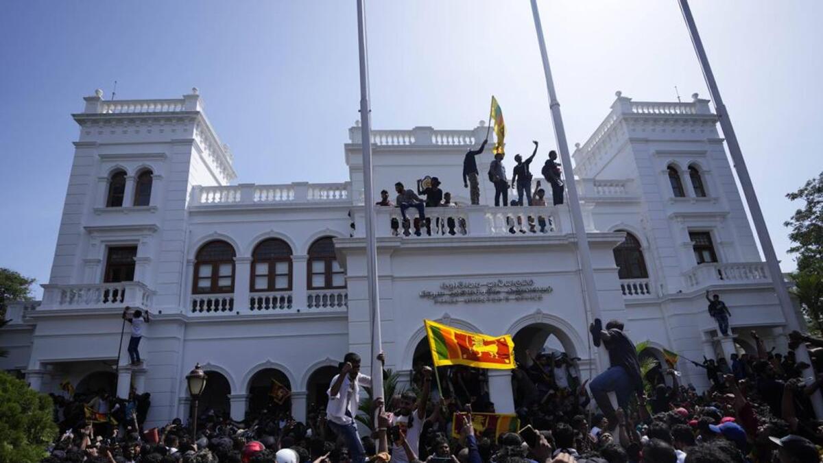 A protester, carrying national flag, stands with others on top of the building of Sri Lankan Prime Minister Ranil Wickremesinghe's office