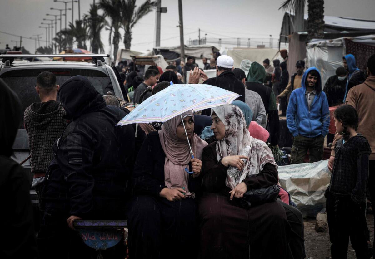 Palestinian women talk under an umbrella at a makeshift camp housing displaced Palestinians in Rafah in the southern Gaza Strip. — AFP