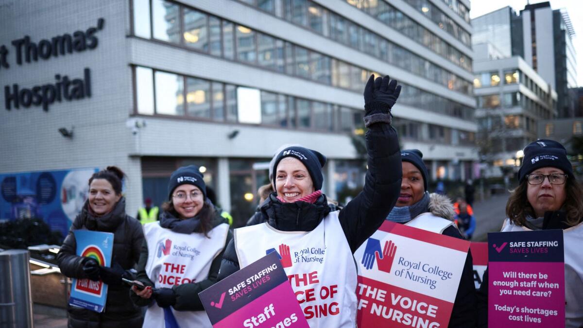 A nurse waves as she and others hold signs during a strike outside St Thomas' Hospital in London. — Reuters