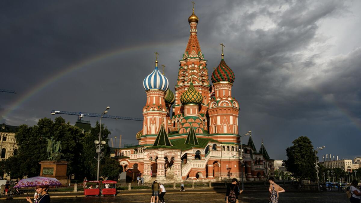 People walk in front of St. Basil Cathedral lit by the sun with a rainbow in the background on Red Square in Moscow. Photo: AFP