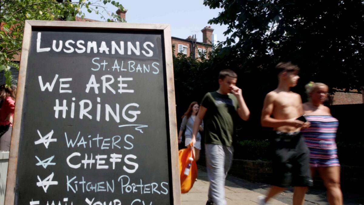 People walk past a sign that announces vacancies after many workers were asked to isolate in Britain following contact with someone with Covid-19. — Reuters