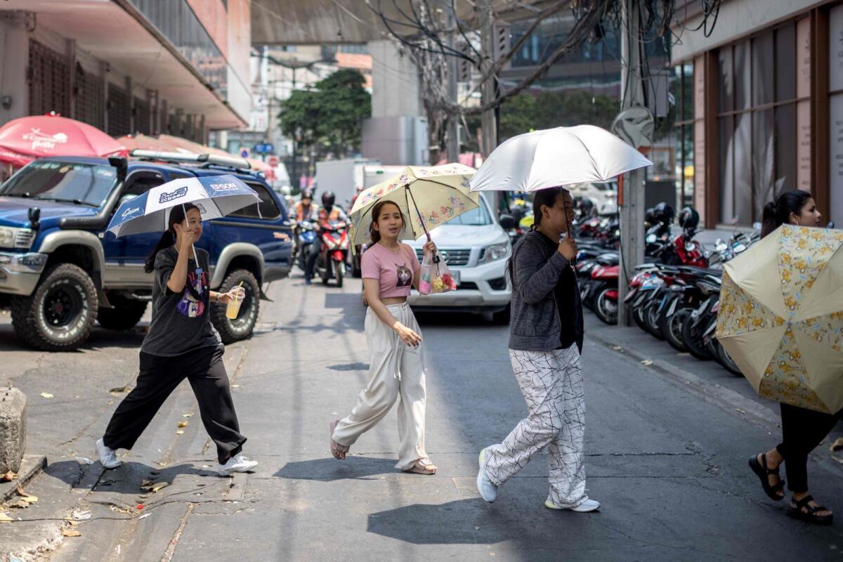 People sheltering from the sun under umbrellas cross a street during heatwave conditions in Bangkok on April 20, 2023. — AFP