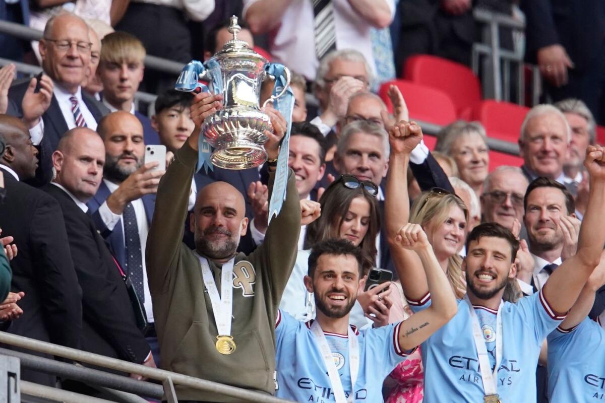 Manchester City head coach Pep Guardiola lifts the trophy as he celebrates with the team after winning the FA Cup final against Manchester United. — AP