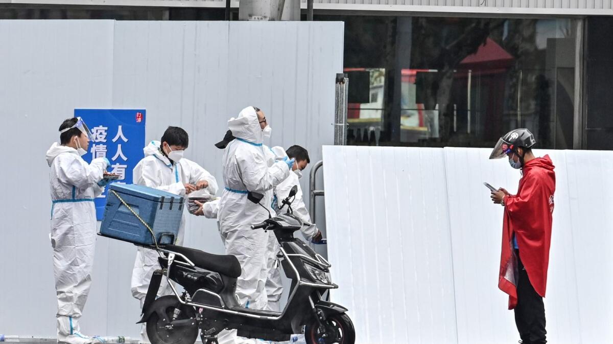 A delivery man (R) is seen next to workers wearing protective gear outside of a locked down neighbourhood after the detection of new cases of Covid-19 in Huangpu district, in Shanghai on March 17, 2022. Photo: AFP