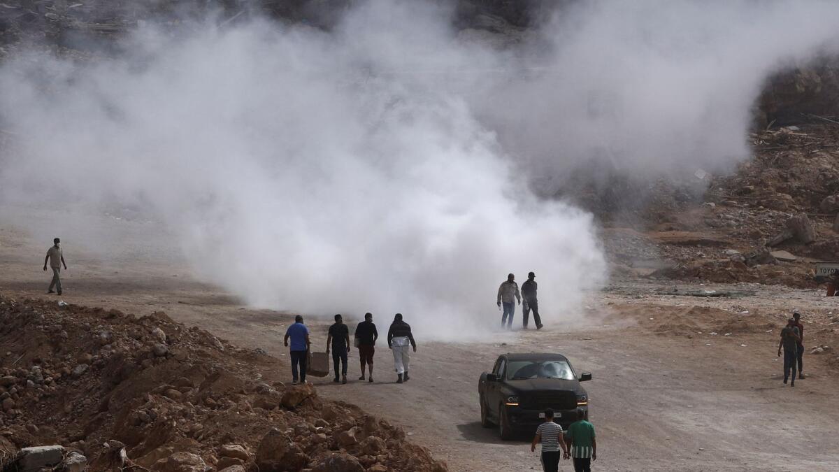 People emerge from smoke caused by a sanitation truck amid rising concerns of the spread of infectious diseases after fatal floods in Derna. — Reuters