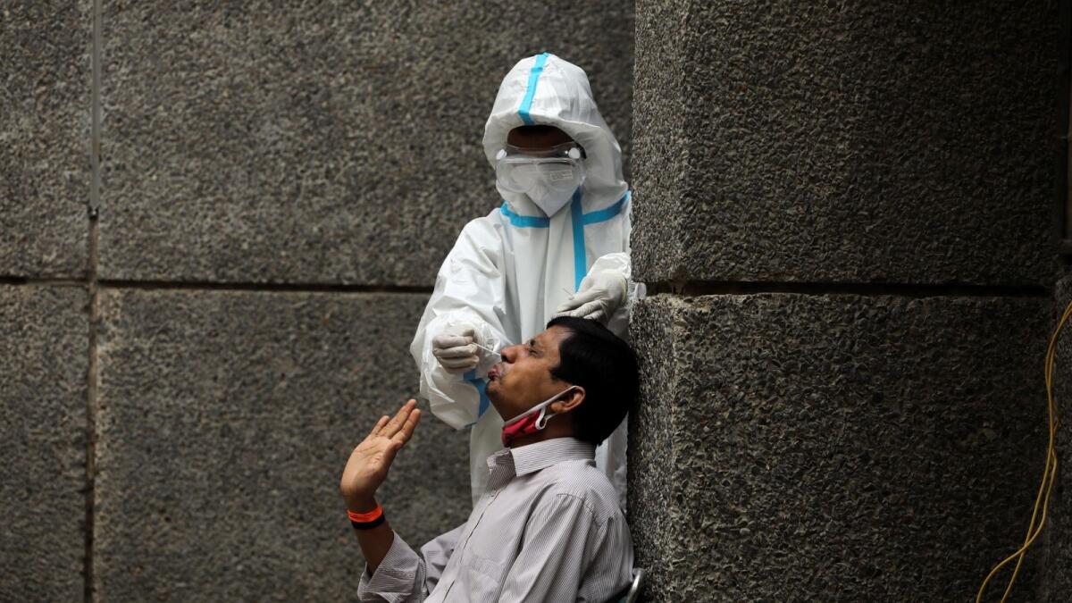 A healthcare worker wearing personal protective equipment (PPE) collects a swab sample from a man amidst the spread of Covid-19, at a testing center in New Delhi, India. Reuters