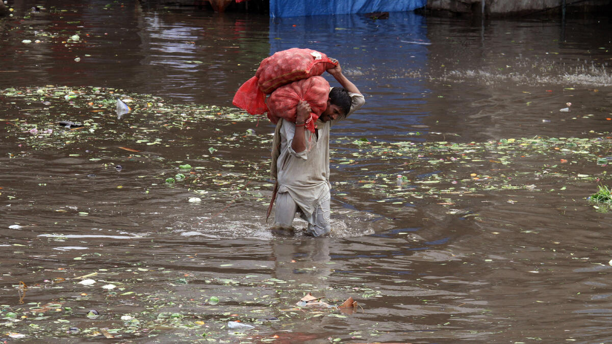 A Pakistani laborer carries sacks of potatoes while he wades through a flooded road caused by heavy rains in Lahore, Pakistan