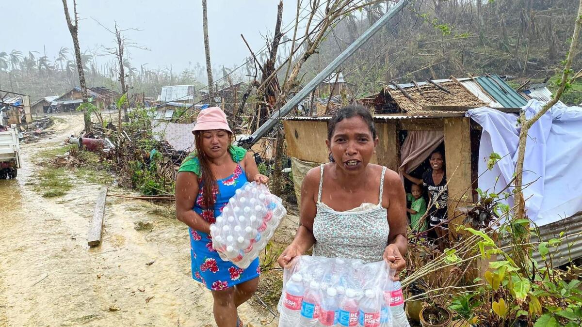 Residents carry bottled water given as aid from a non-governmental organisation in Burgos town, Philippines. – AFP