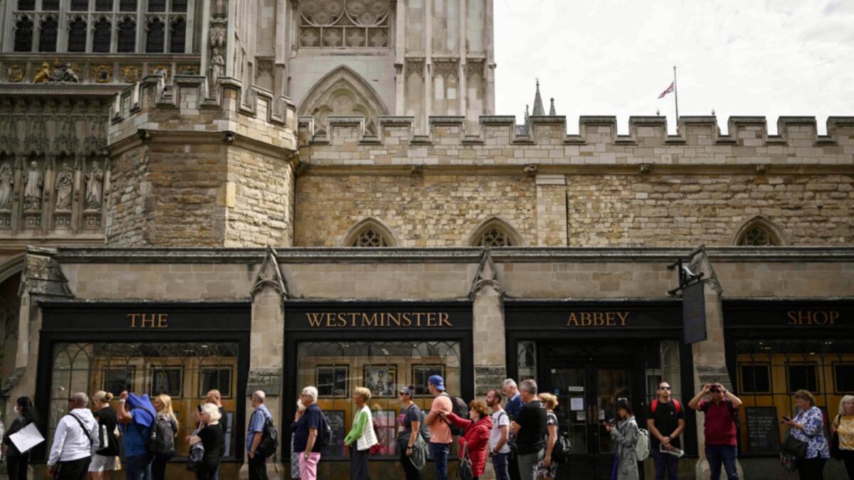 Pictures of Britain's Queen Elizabeth II are seen as people queue to enter the Westminster Abbey. — AFP