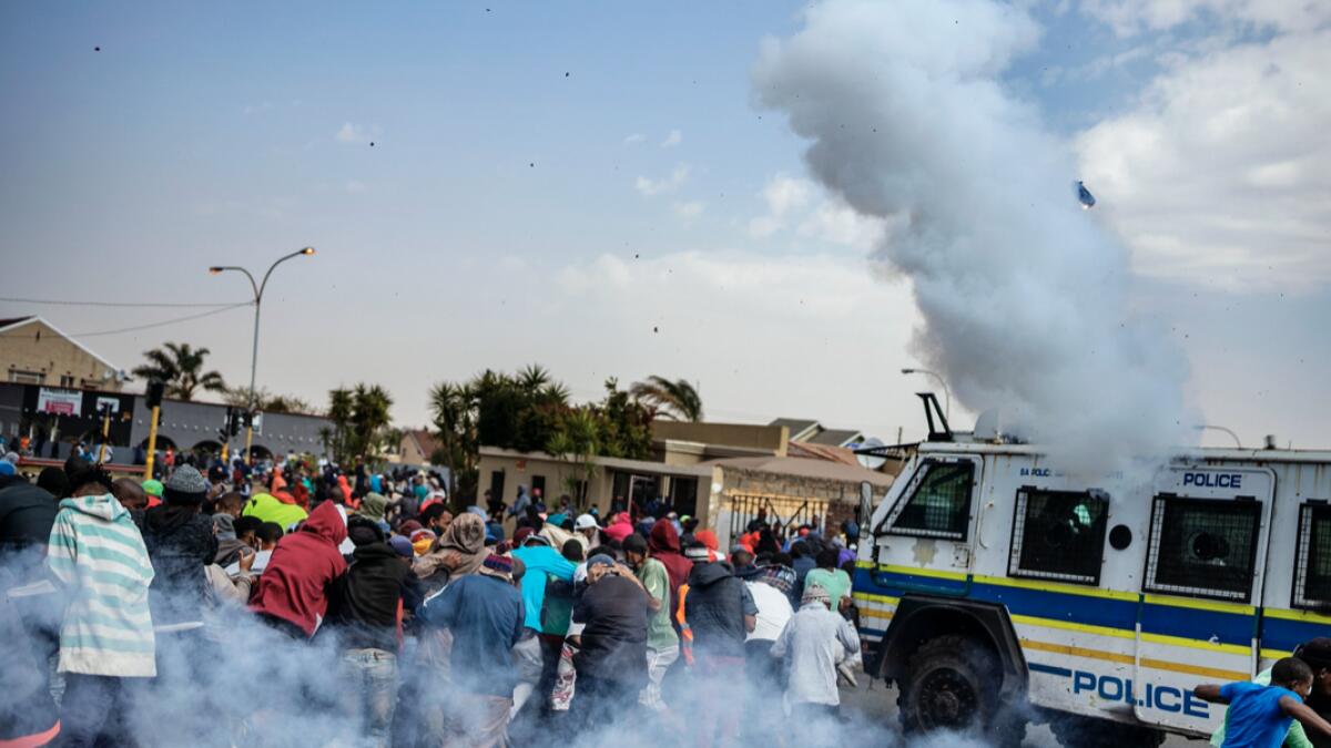 Residents run from a stun grenade thrown by a member of the South African Police Service (SAPS) outside the SAPS offices in Eldorado Park, near Johannesburg, during a protest by community members after a 16-year old boy was reported dead. Photo: AFP