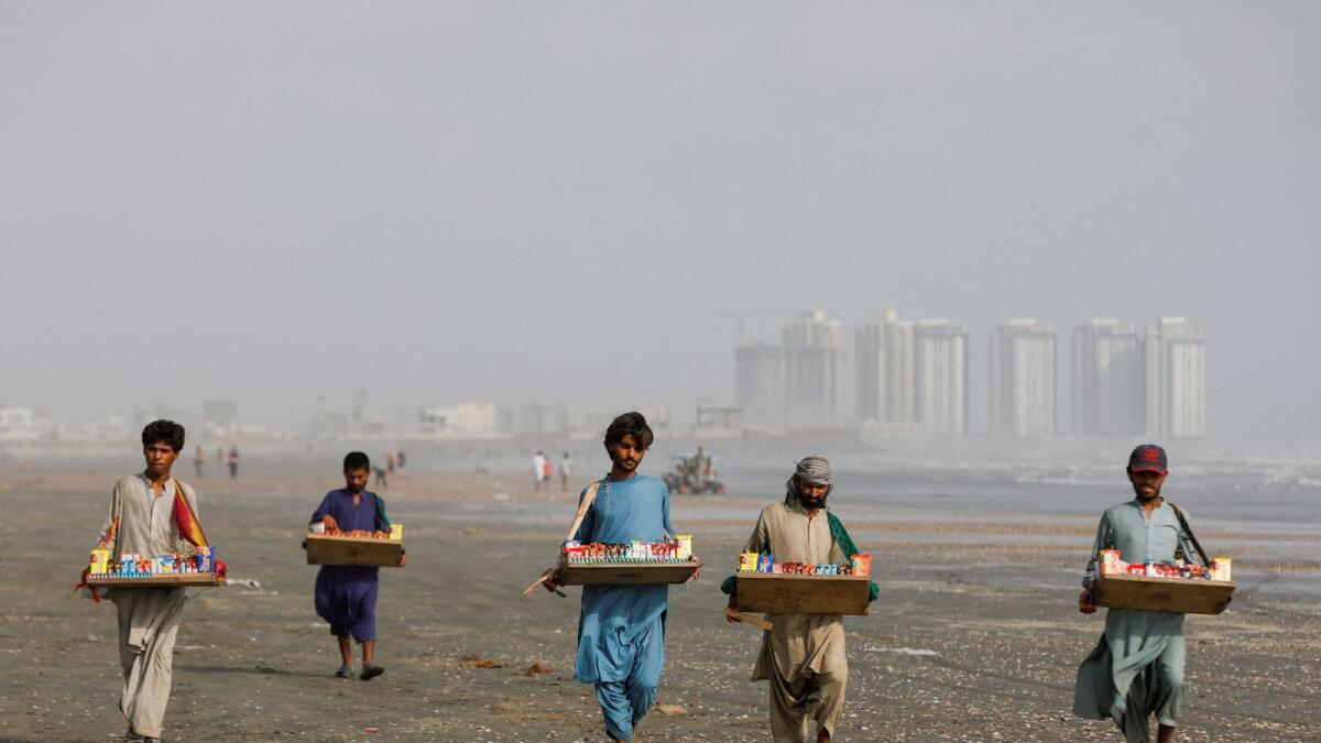 People, who moved to Karachi from Pakistan's southwestern province of Balochistan to look for work, walk with trays of sundries as they sell them along Clifton Beach in Karachi, Pakistan, on Tuesday. —  Reuters