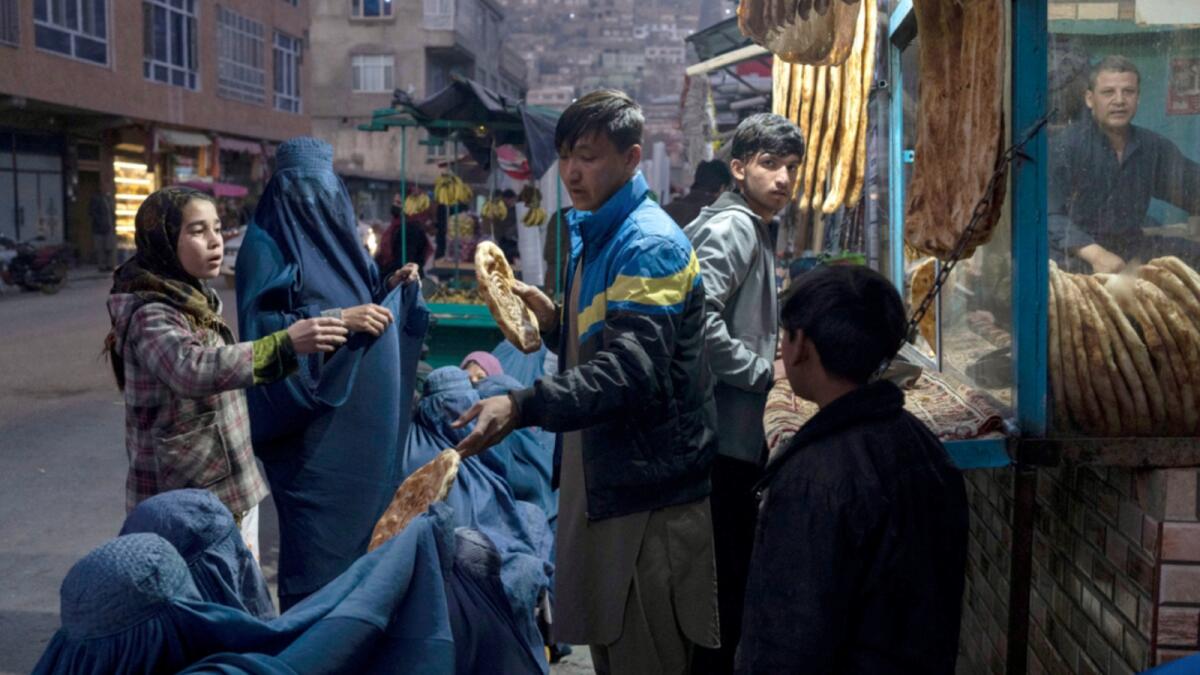 A man distributes bread to Burka-wearing Afghan women outside a bakery in Kabul. — AP