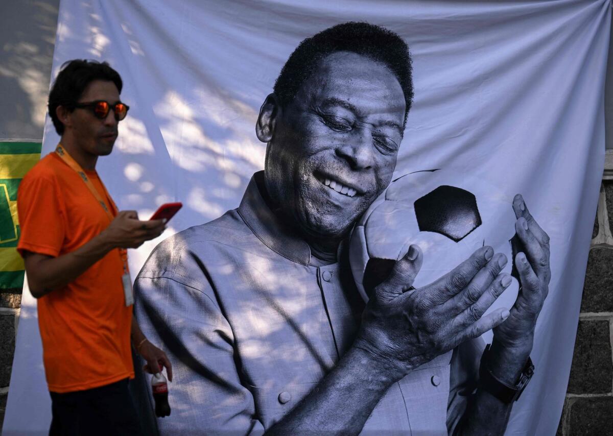 A mourner passes by a piece of cloth with an image of Brazilian football legend Pele outside the Urbano Caldeira stadium, also known as Vila Belmiro, in Santos, Brazil. — AFP