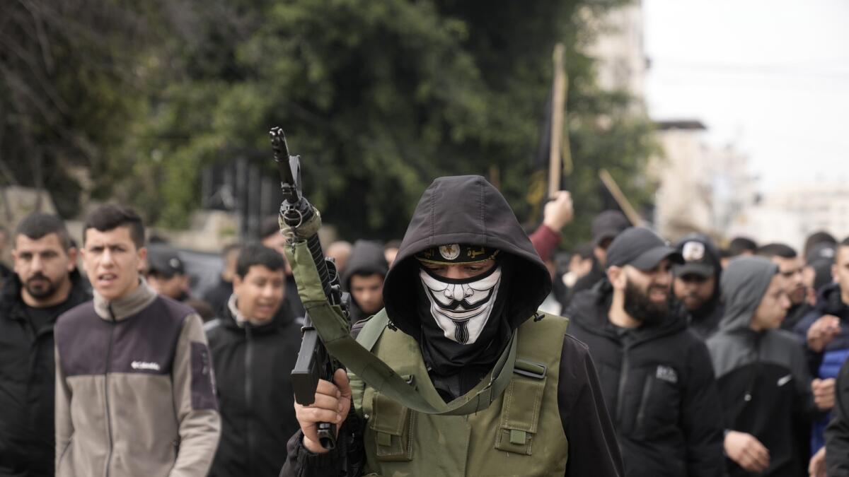 A masked gunman marches alongside of the bodies of Said Jaradat and Yasser Hanoun, both draped in the flag of the Islamic Jihad militant group on Friday. The pair were killed in an Israeli drone strike on a car in the West Bank Jenin refugee camp a day earlier. — AP