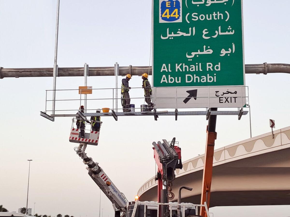 Workers replace a traffic signboard on a Dubai road. — Supplied photo