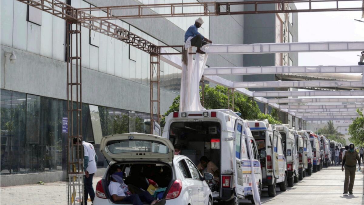 Ambulances carrying Covid-19 patients wait for their turn to be attended outside a government hospital  in Ahmedabad as a worker erects a sun shade. — AP