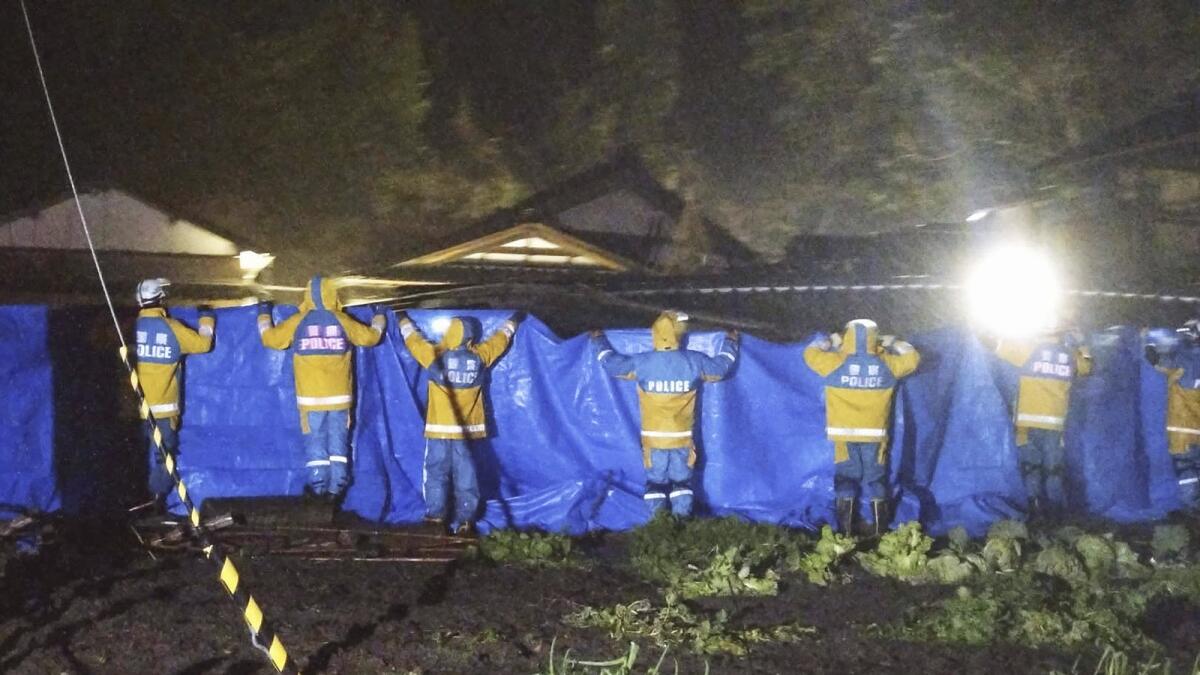 Police officers use blue sheets as a woman in 90s is rescued alive from a collapsed house in Suzu. — AP