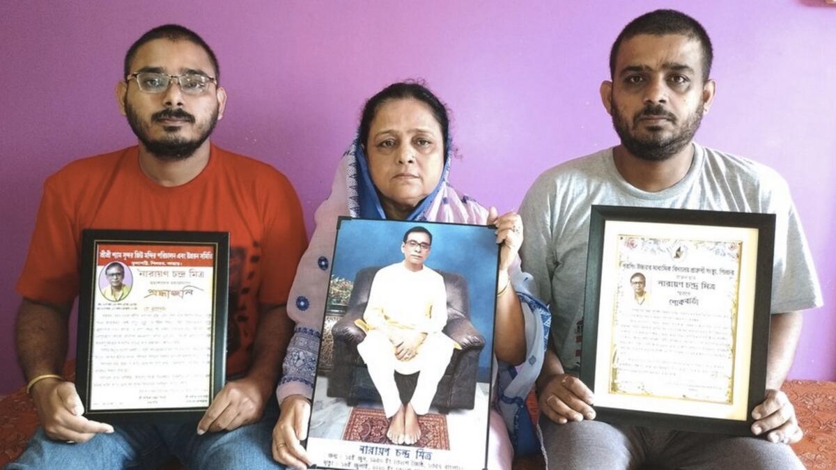 Anindita Mitra, 61, flanked by her sons Satyajit Mitra, right and Abhijit Mitra, pose with portraits of her husband late Narayan Mitra, at her house in Silchar, India. AP