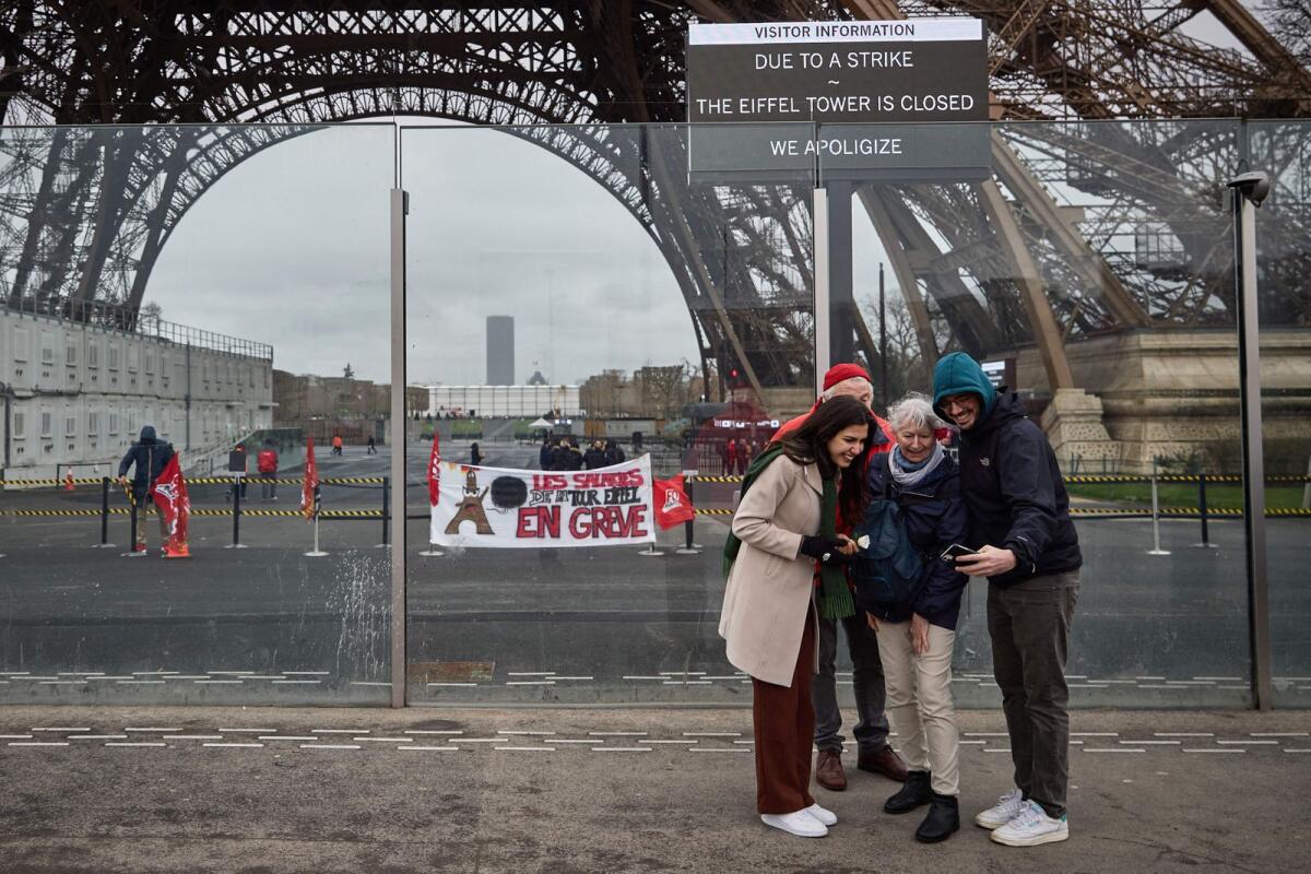 Pedestrians take a picture next to the Eiffel Tower, and a board (Top R) informing visitors that the monument is closed as staff go on strike, and a displayed banner (C) reading 'employees of the Eiffel Tower on strike' in Paris on Monday. — AFP