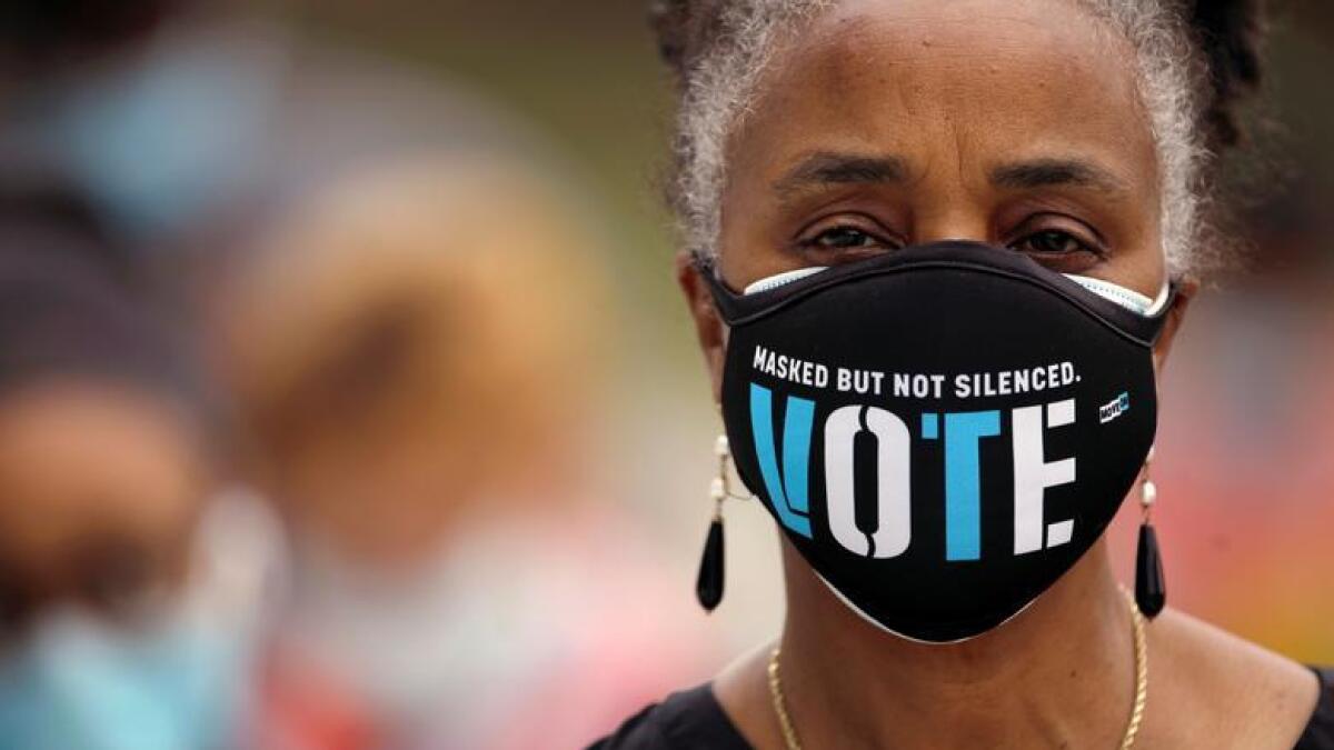 A woman wears a mask with a message urging voter participation while she waits in line to enter a polling place on the first day of the state's in-person early voting for the general election in Durham, North Carolina.